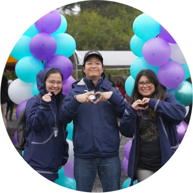 Three women employees outside at an event, making hearts with their hands.